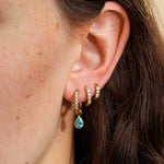 Close-up of an ear wearing gold hoop earrings with a blue teardrop earring.