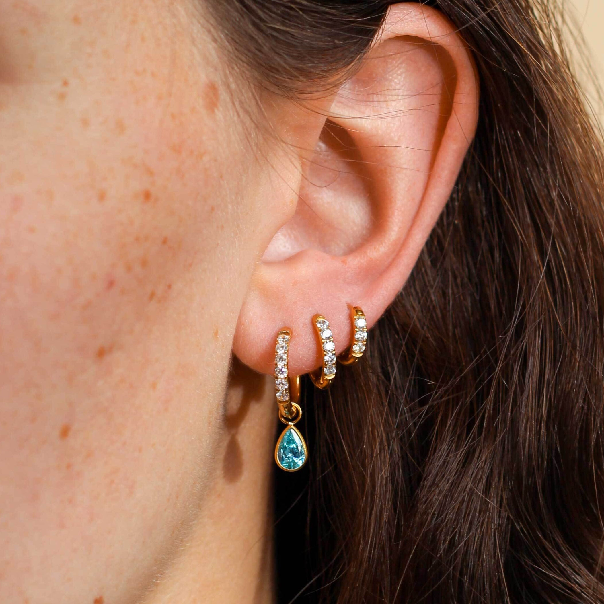 Close-up of an ear wearing gold hoop earrings with a blue teardrop earring.