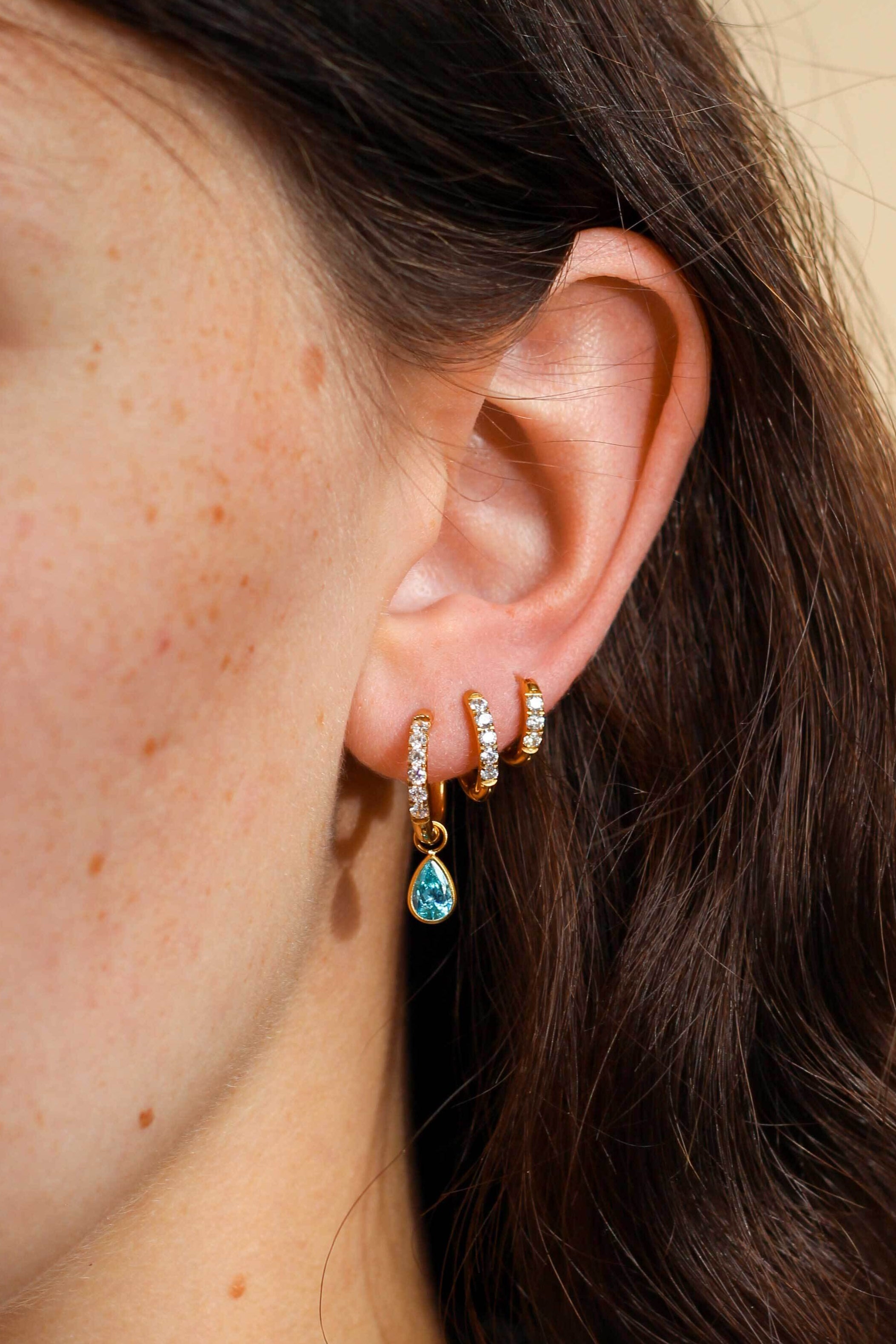 Close-up of an ear wearing gold hoop earrings with a blue teardrop earring.