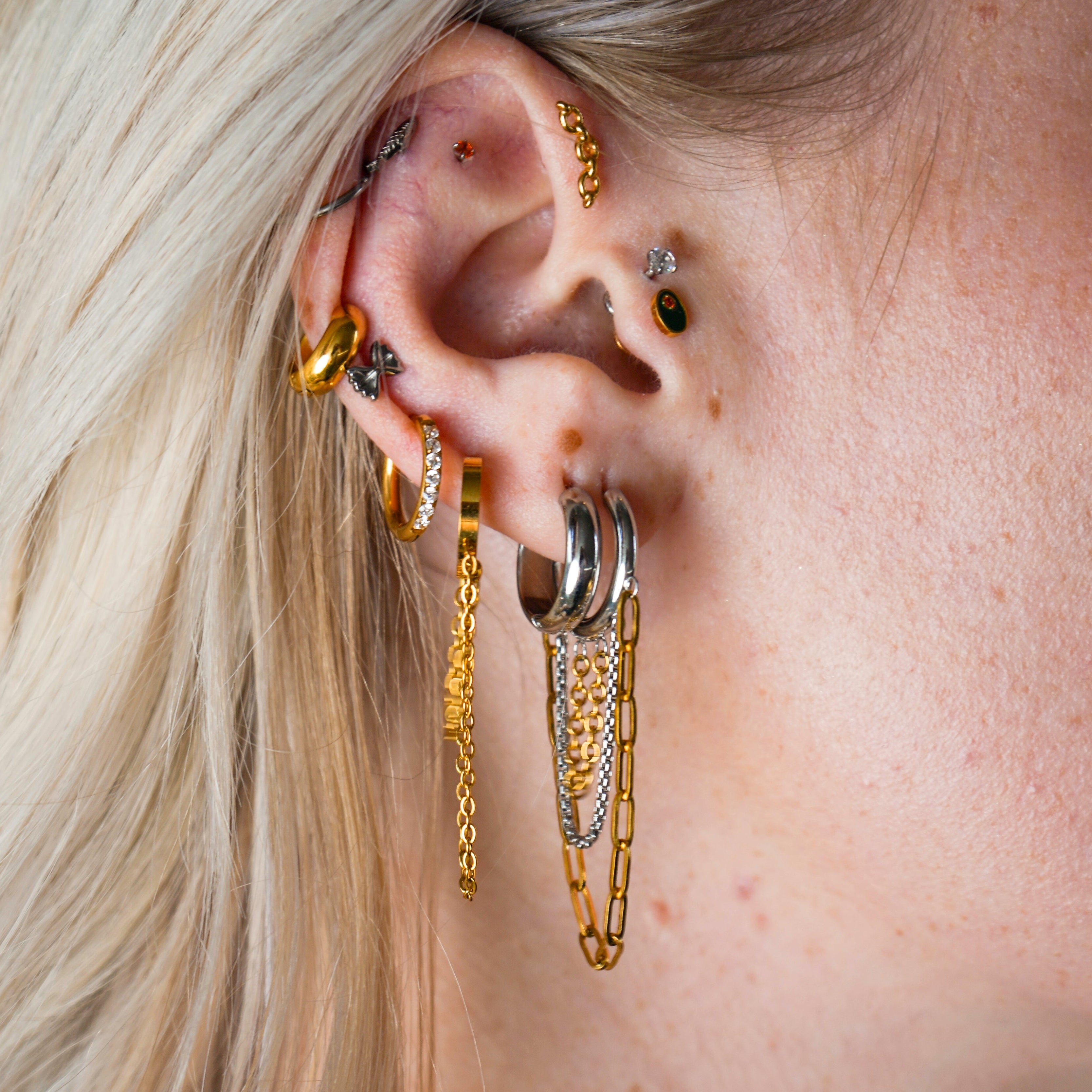 Close-up of an ear with multiple gold hoop earrings and a blurred background