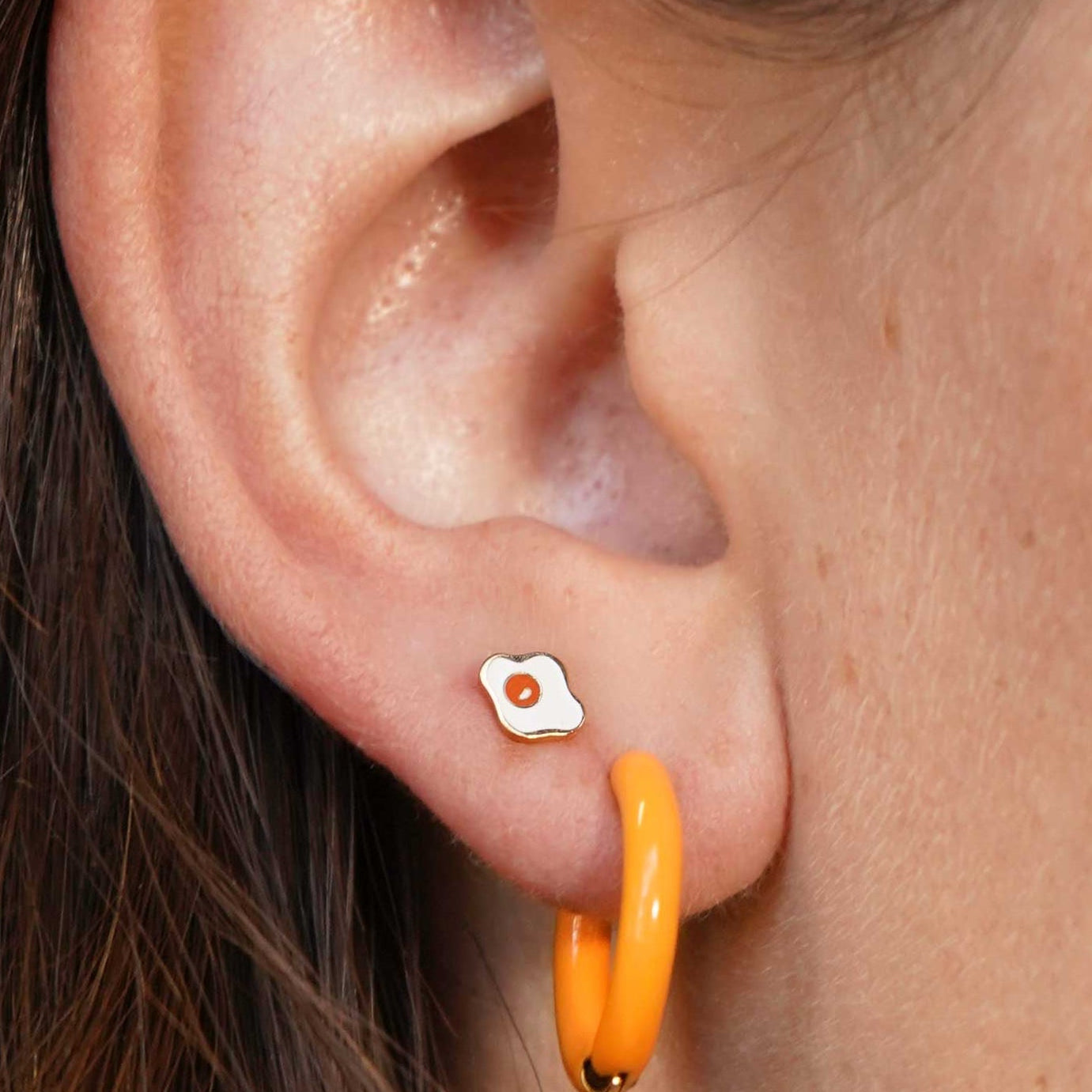Close-up of an ear with a small earring and a larger orange hoop earring.