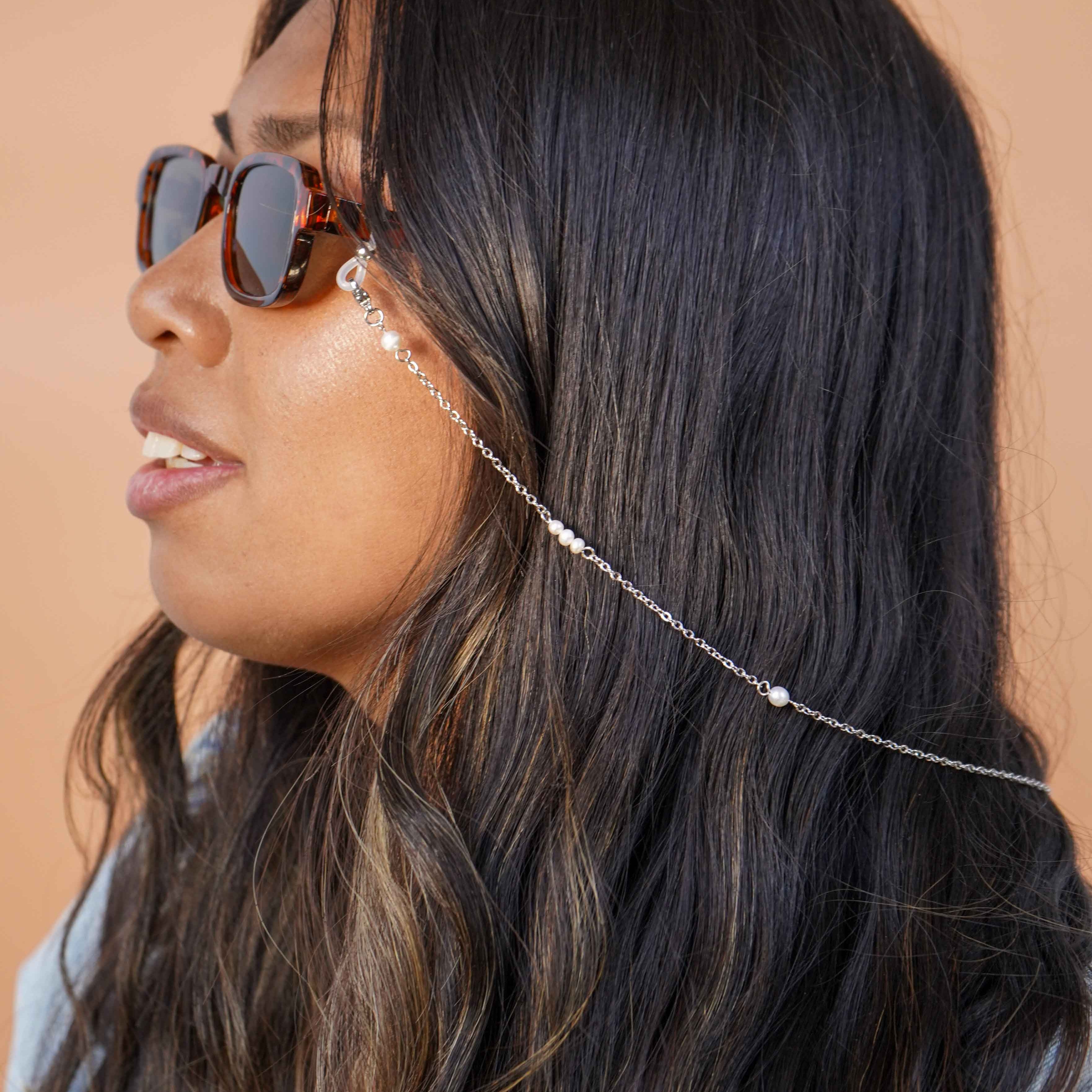 Woman wearing sunglasses with a silver glasses chain accessory against a beige background