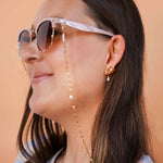Woman wearing sunglasses with a gold chain, against a beige background