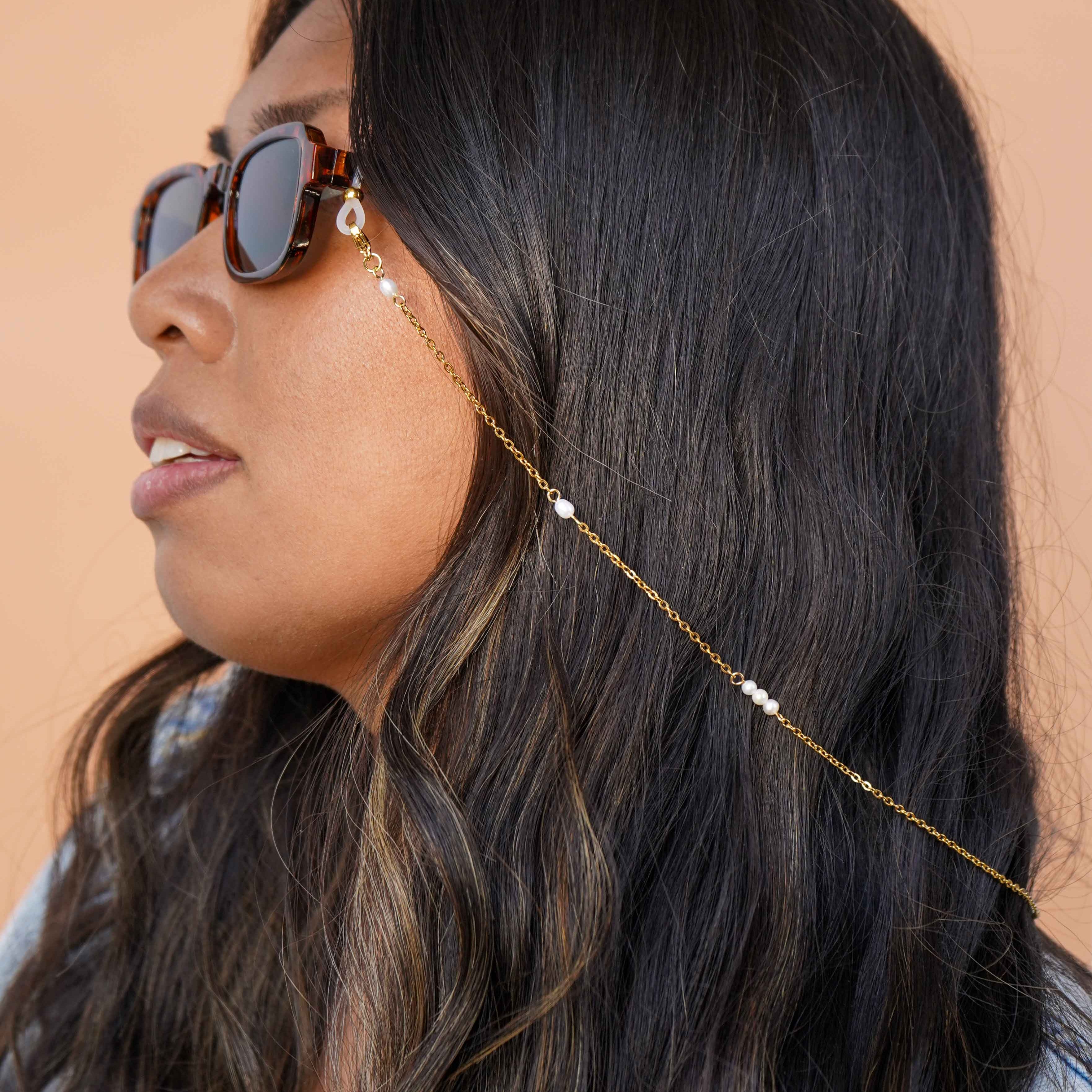 Woman wearing sunglasses with a gold glasses chain accessory against a beige background