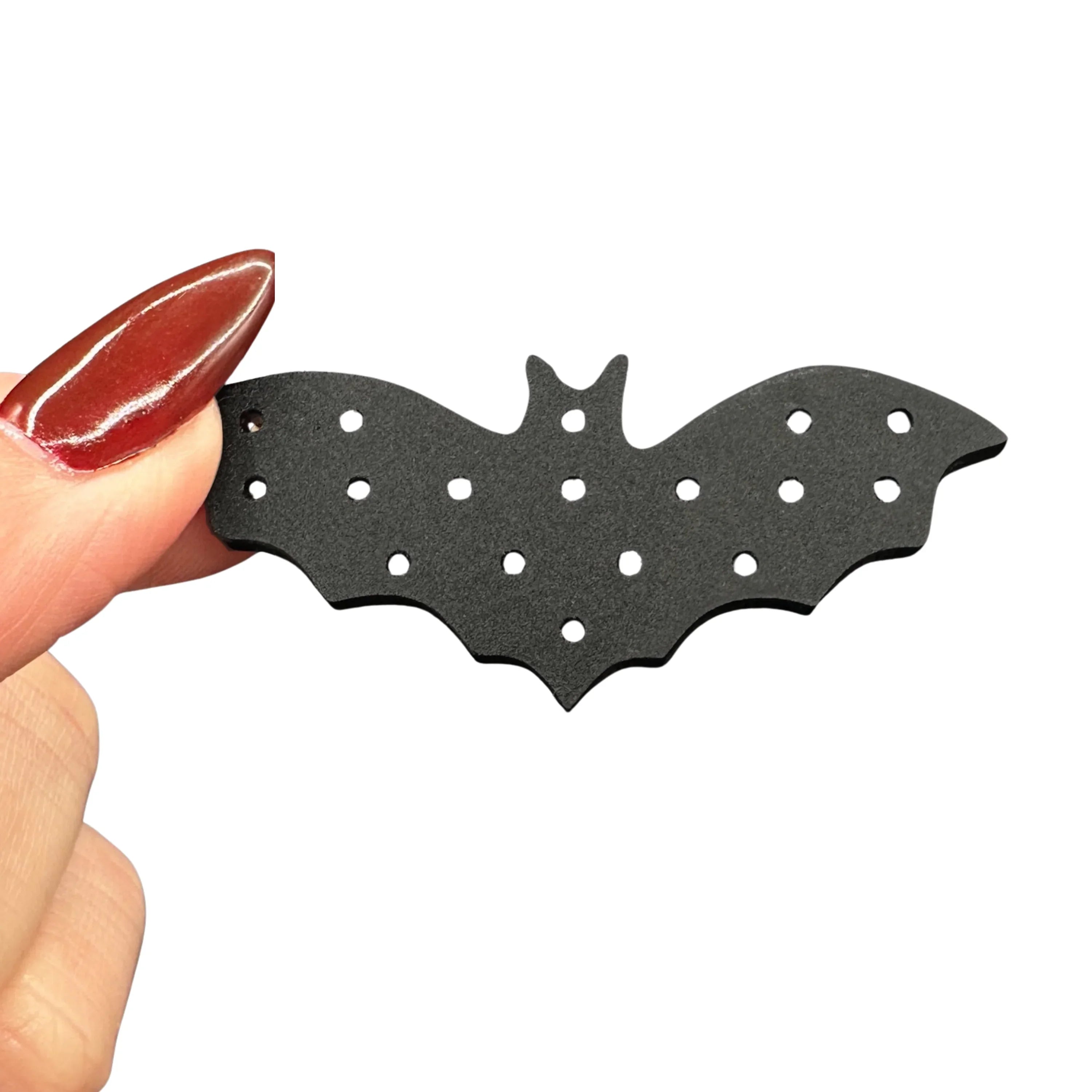 Black bat-shaped acrylic organizer for small earrings, held by a hand with red nail polish on a white background