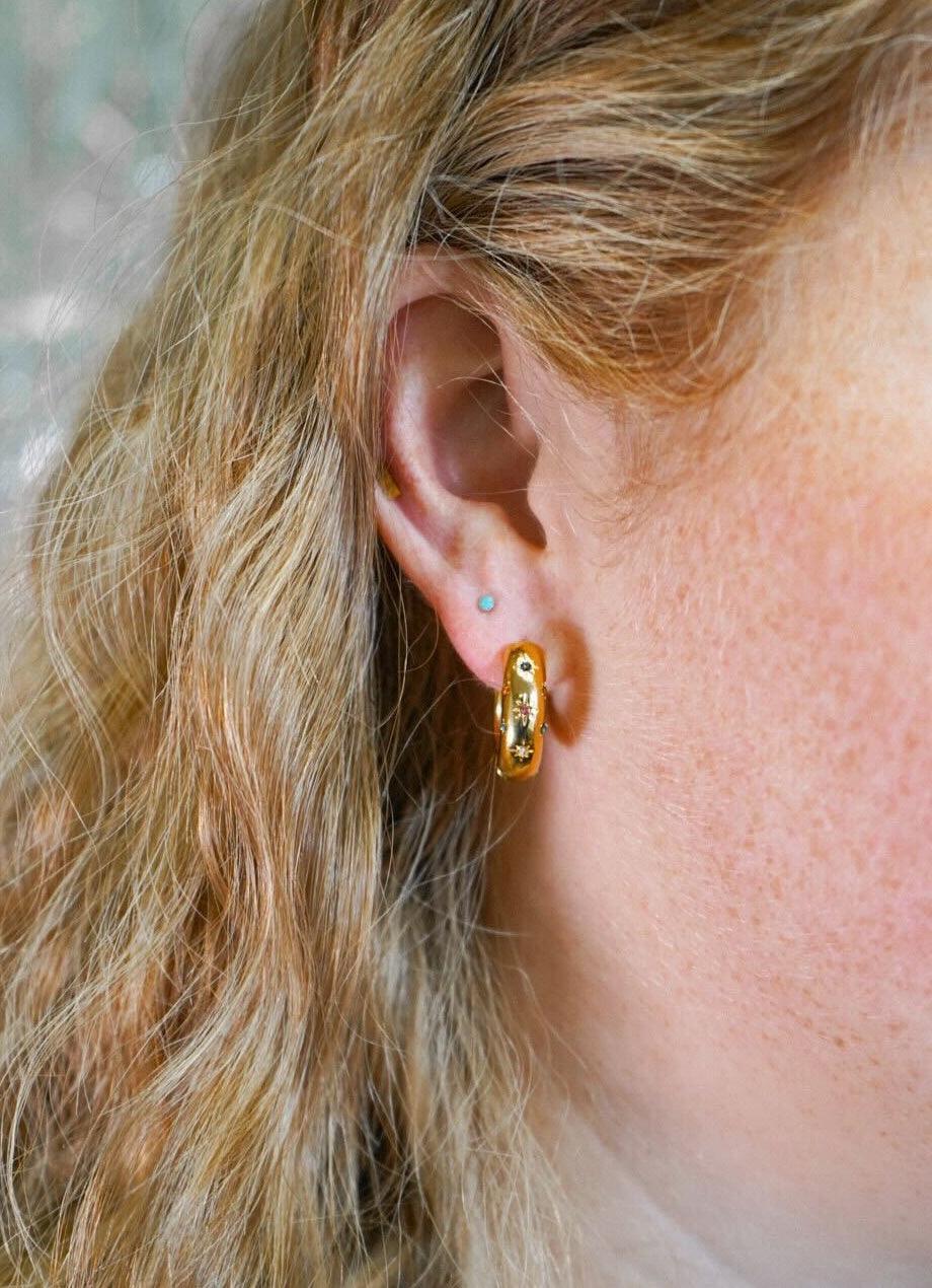 Close-up of a person wearing a gold hoop earring with a blurred background