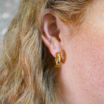 Close-up of a person wearing a gold hoop earring with a blurred background