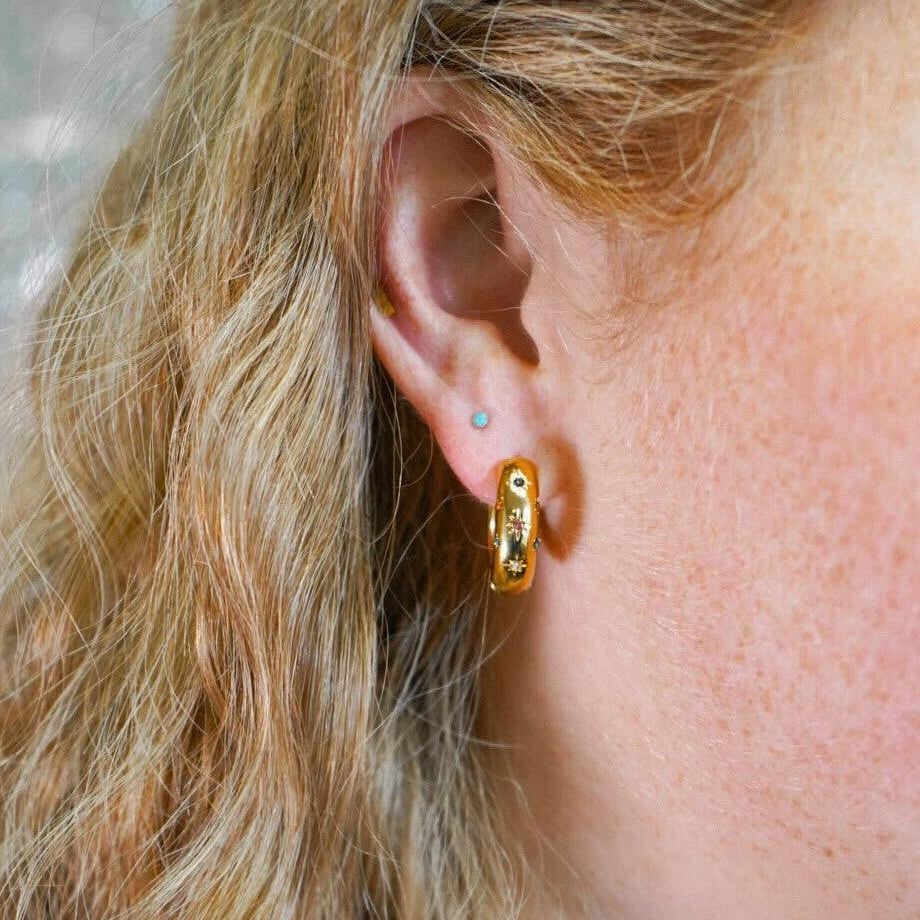 Close-up of a person wearing a gold hoop earring with a blurred background