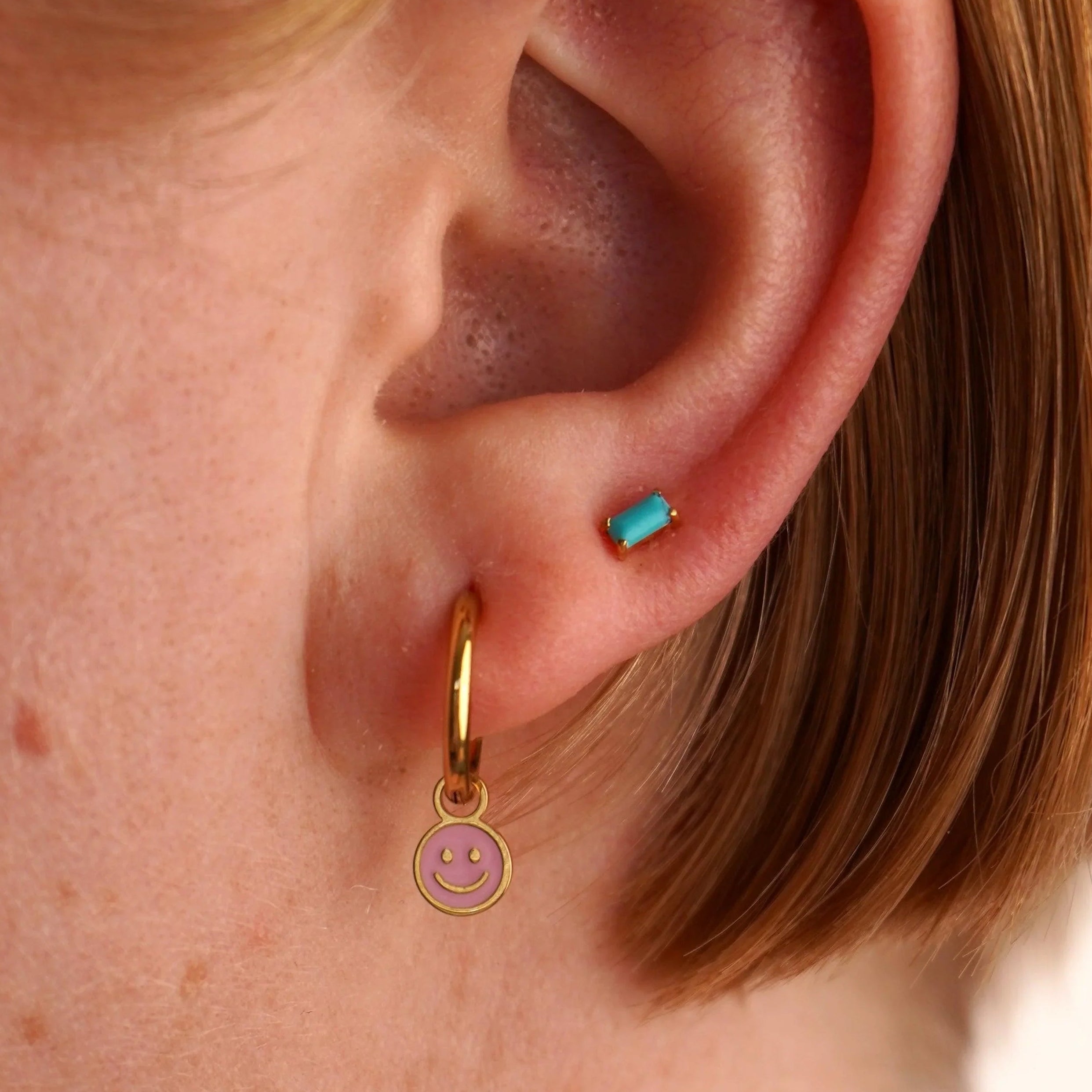 Close-up of an ear with a gold hoop earring featuring a smiley face charm.