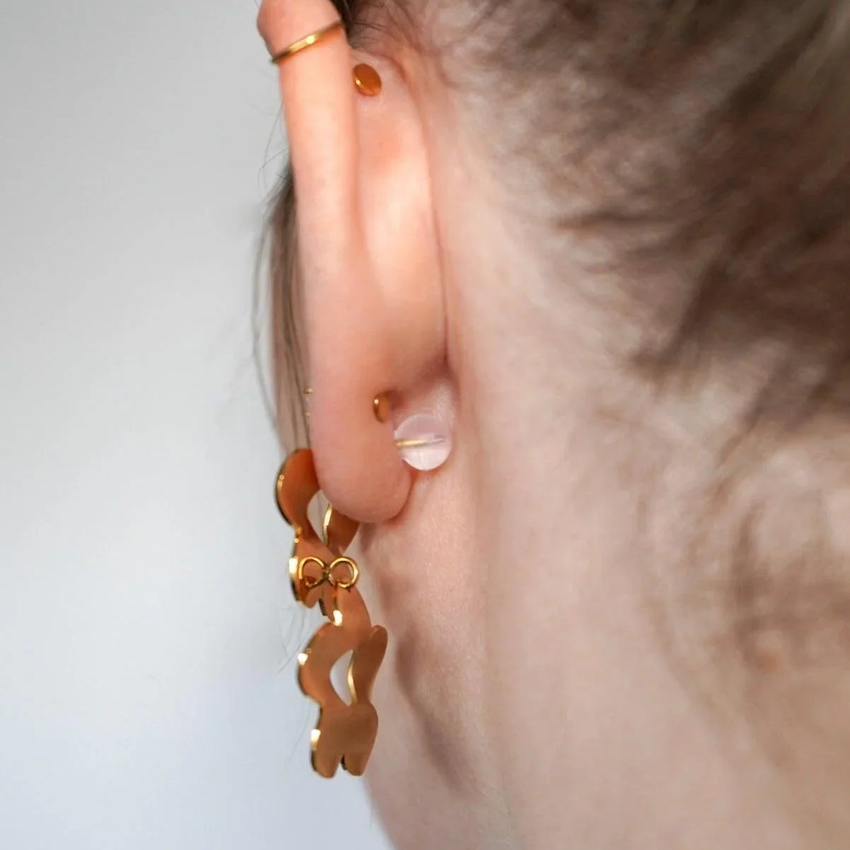 Close-up of an ear wearing a gold earring against a neutral background