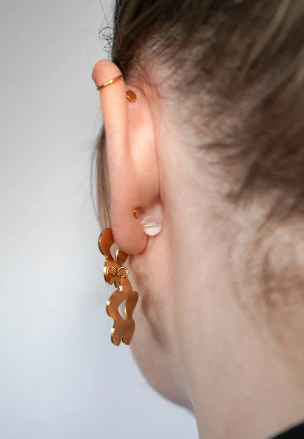 Close-up of an ear wearing a gold earring against a neutral background