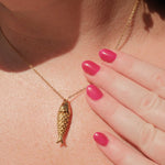 Gold necklace with a fish pendant worn by a person with pink nail polish.