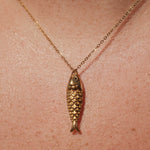 Gold fish-shaped pendant necklace on a person's neck