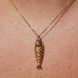 Gold fish-shaped pendant necklace on a person's neck