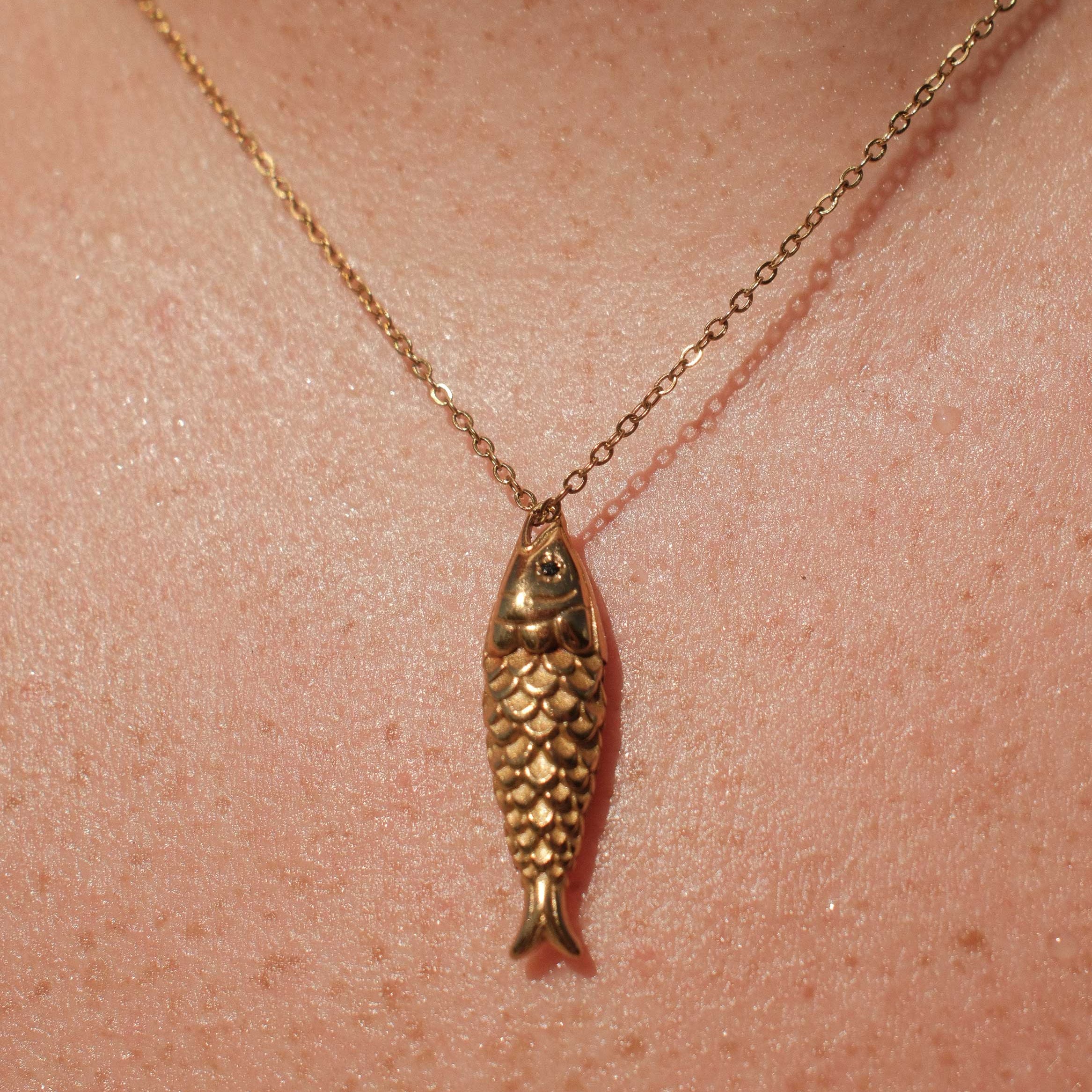 Gold fish-shaped pendant necklace on a person's neck
