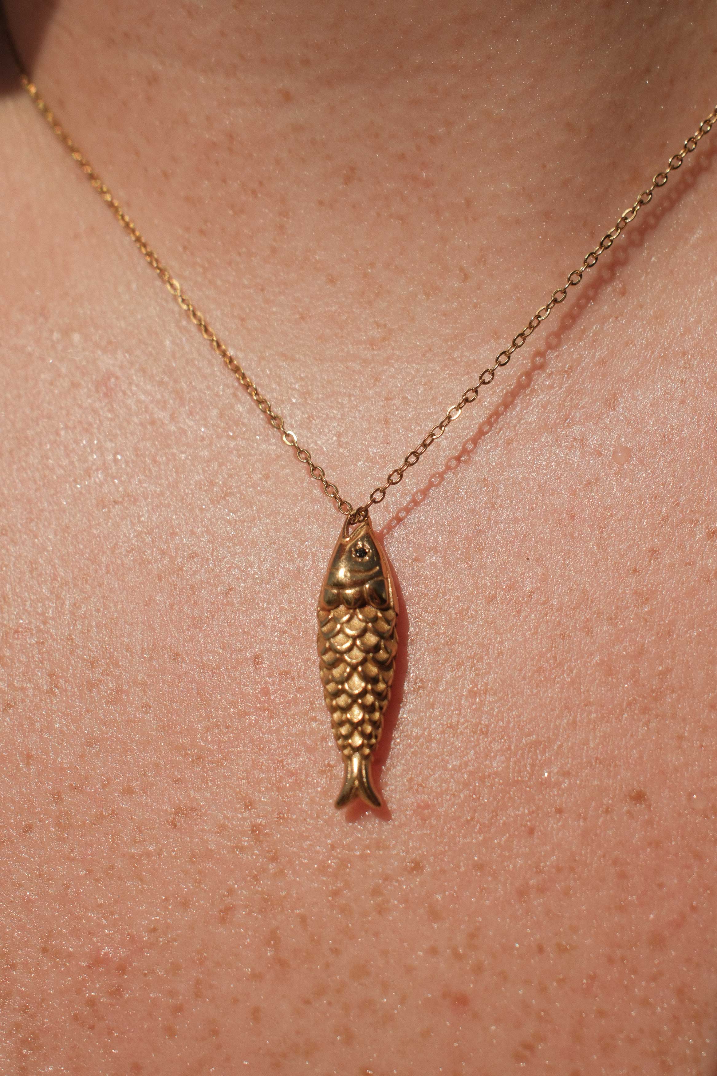 Gold fish-shaped pendant necklace on a person's neck