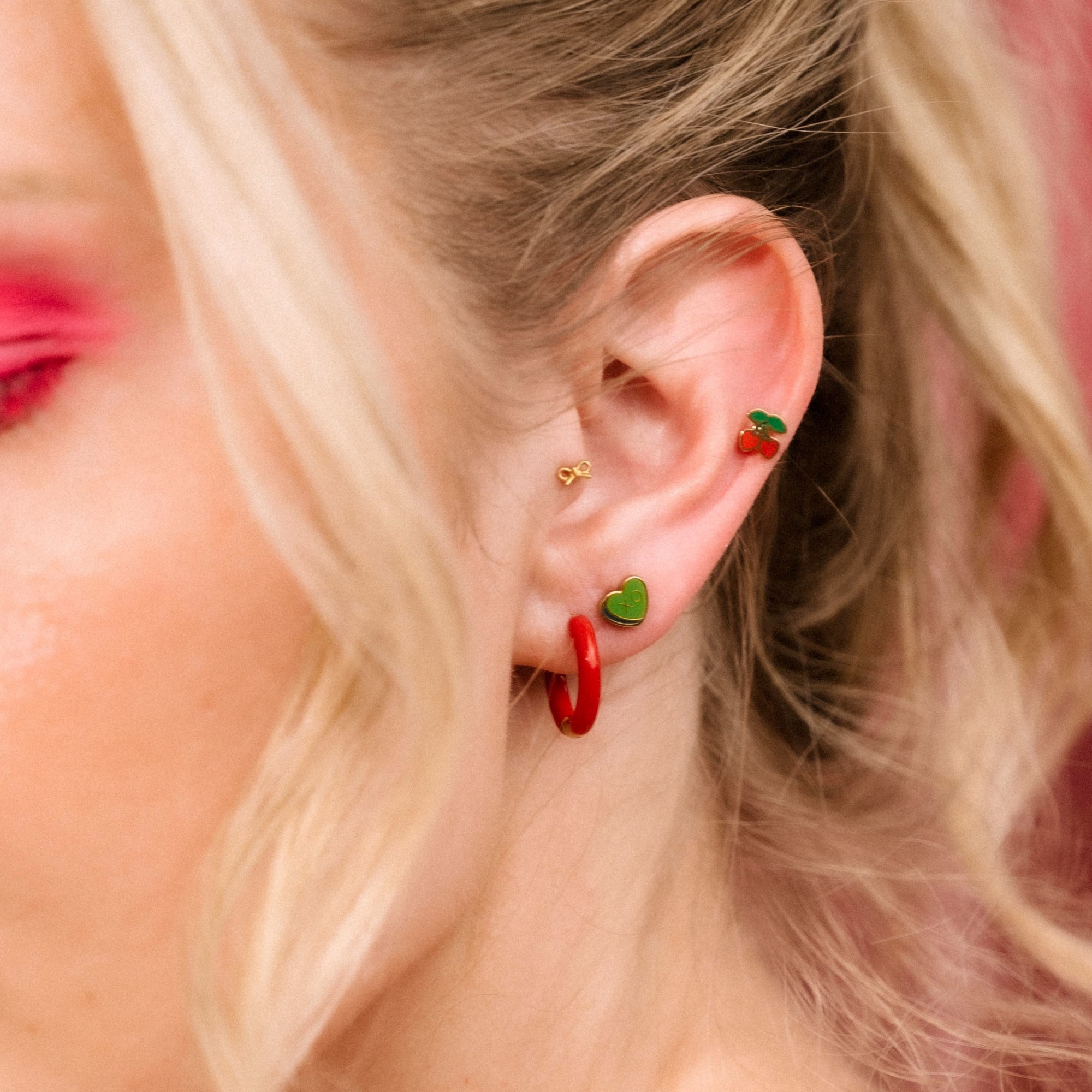 Close-up of a person wearing earrings with green and red accents.
