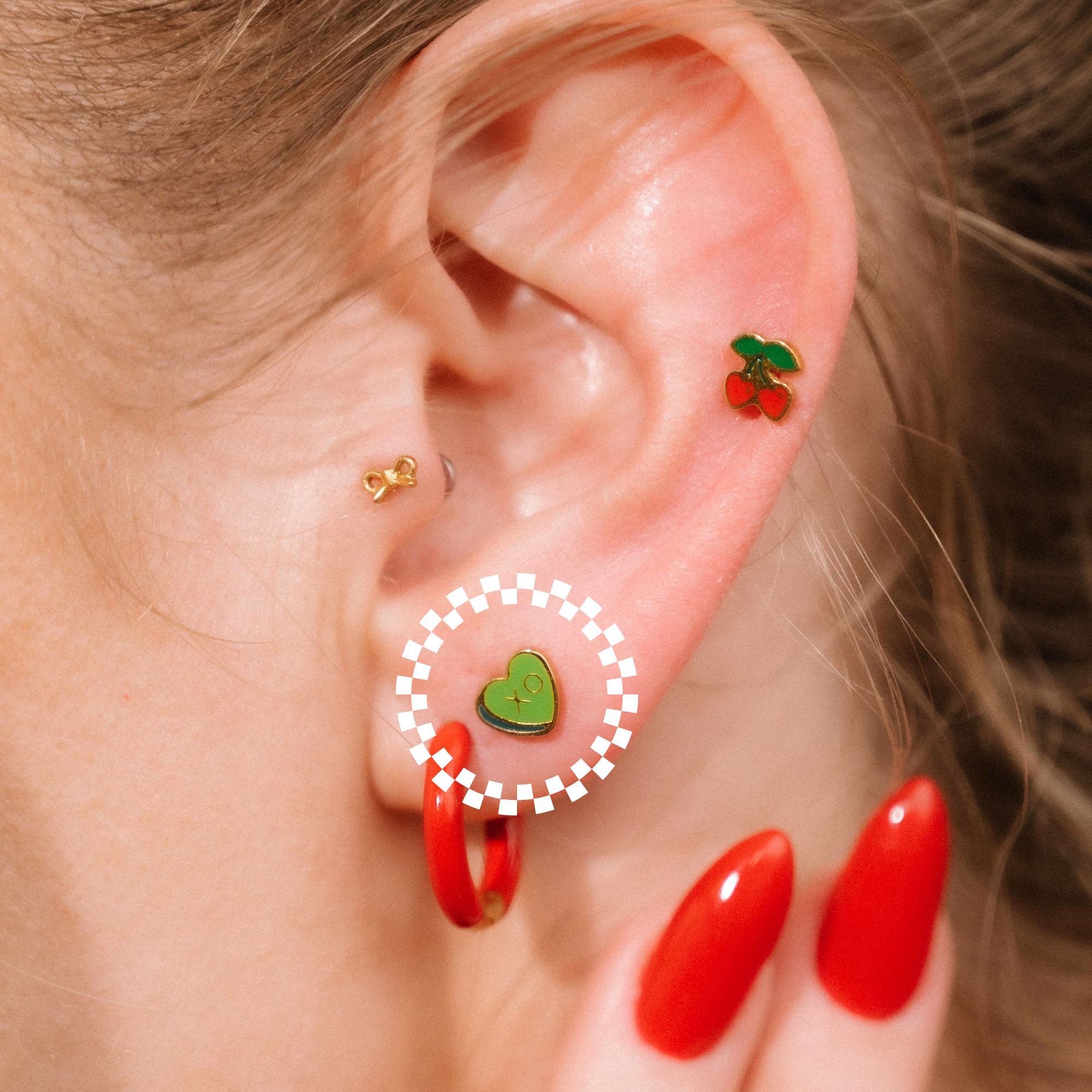 Close-up of an ear with colorful earrings and red nail polish.