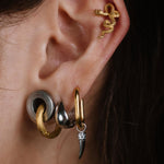 Close-up of a person's ear showcasing multiple stacked and cartilage piercings, including gold hoop, silver and gold cartilage studs, and a small silver drop with a clear stone.