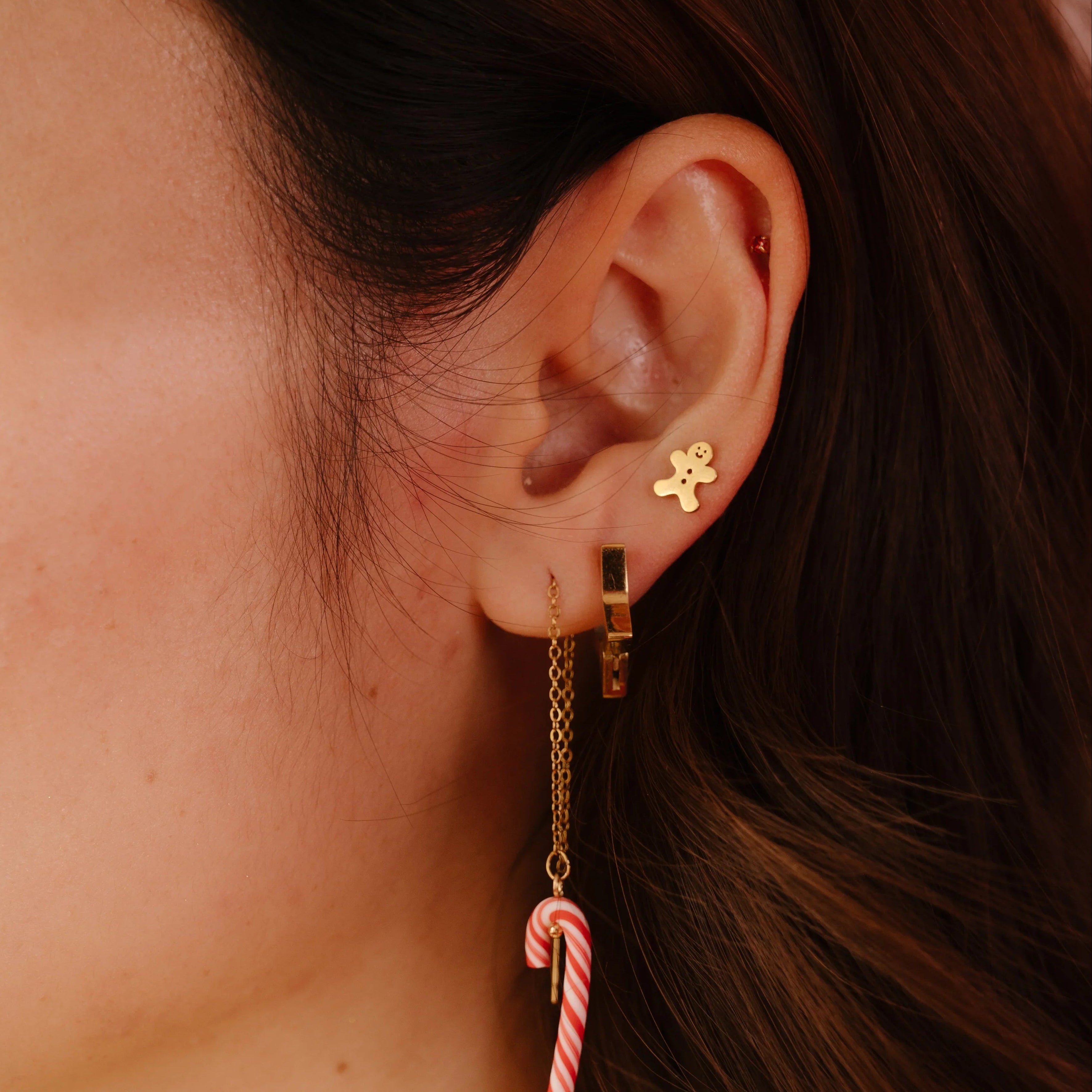 Close-up of an ear wearing a gold earring with a candy cane design.