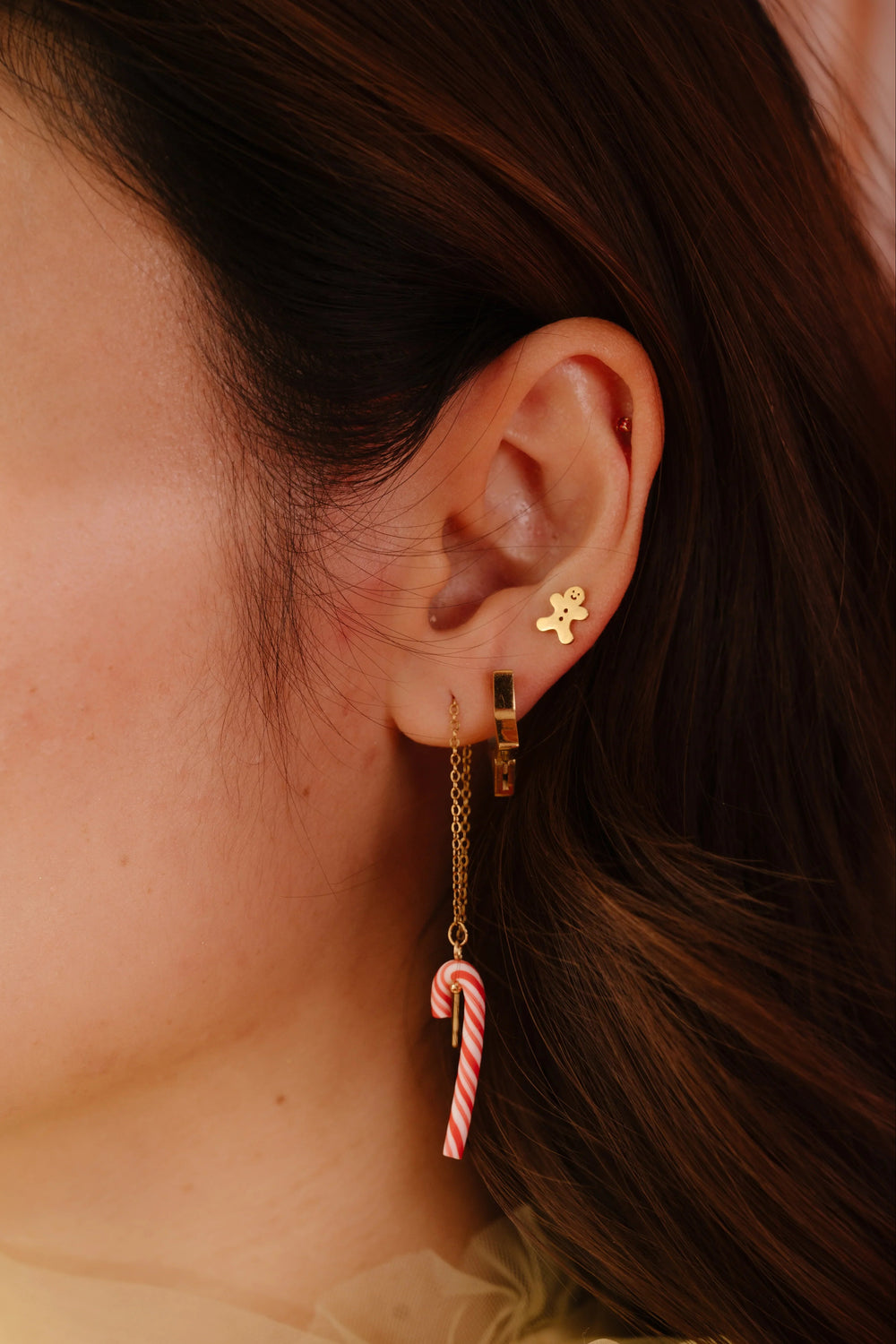 Close-up of an ear wearing a gold earring with a candy cane design.