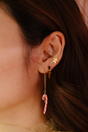 Close-up of an ear wearing a gold earring with a candy cane design.