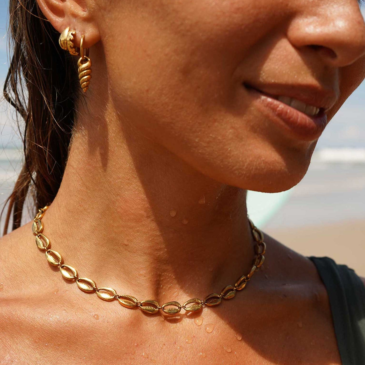 Woman wearing a gold choker necklace and earring on a beach