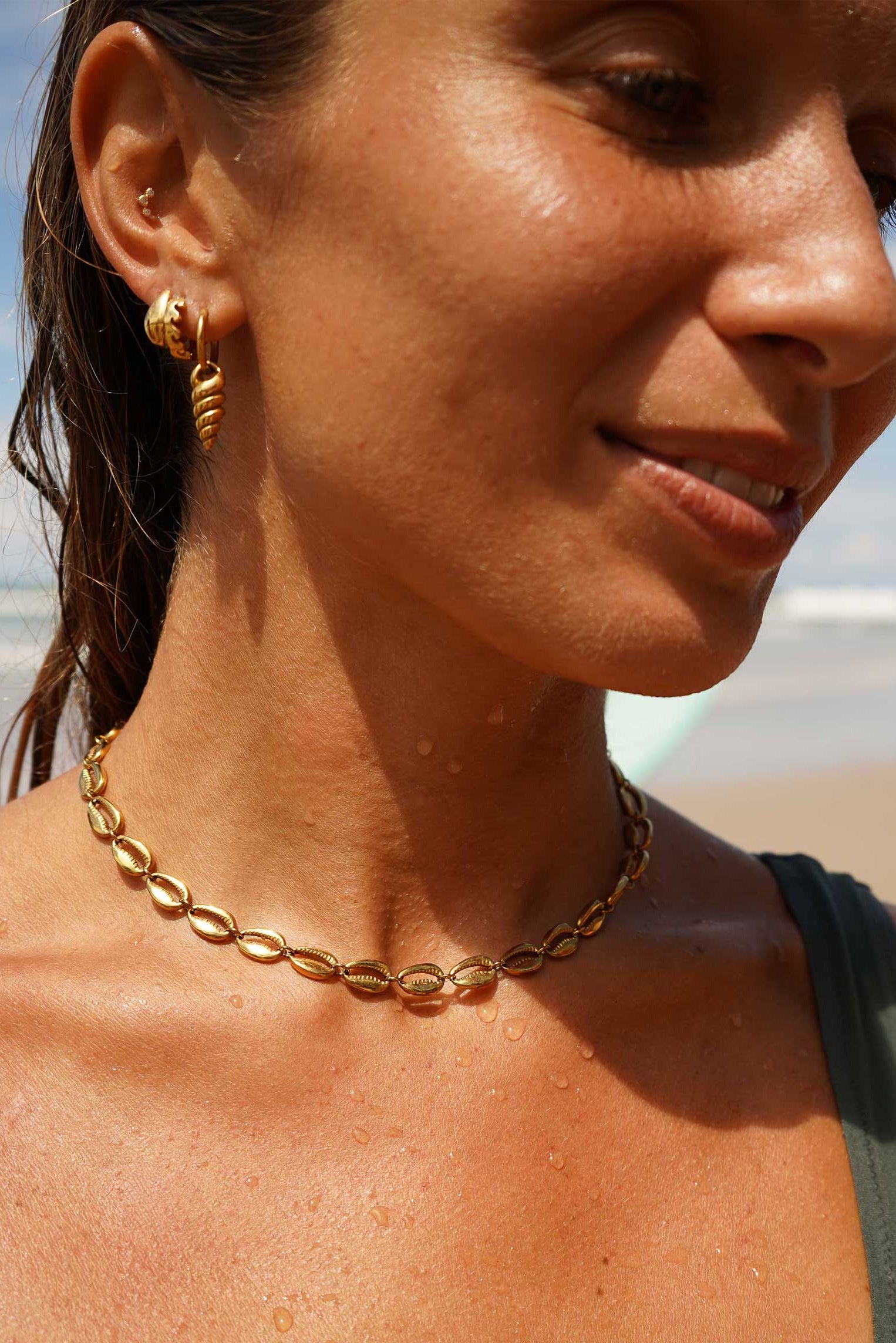 Woman wearing a gold choker necklace and earring on a beach
