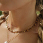 Close-up of a person wearing a gold chain necklace with a pearl pendant.