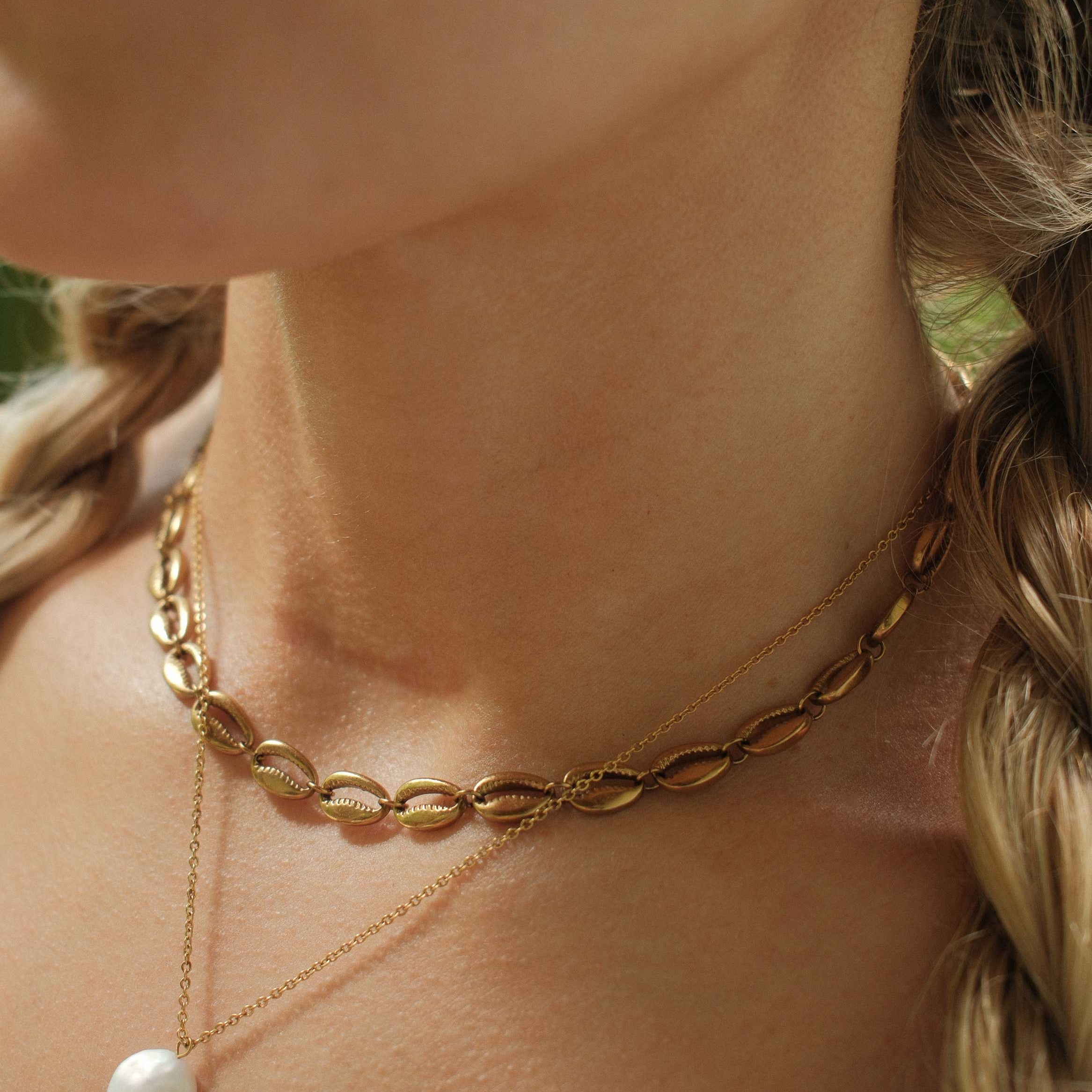 Close-up of a person wearing a gold chain necklace with a pearl pendant.