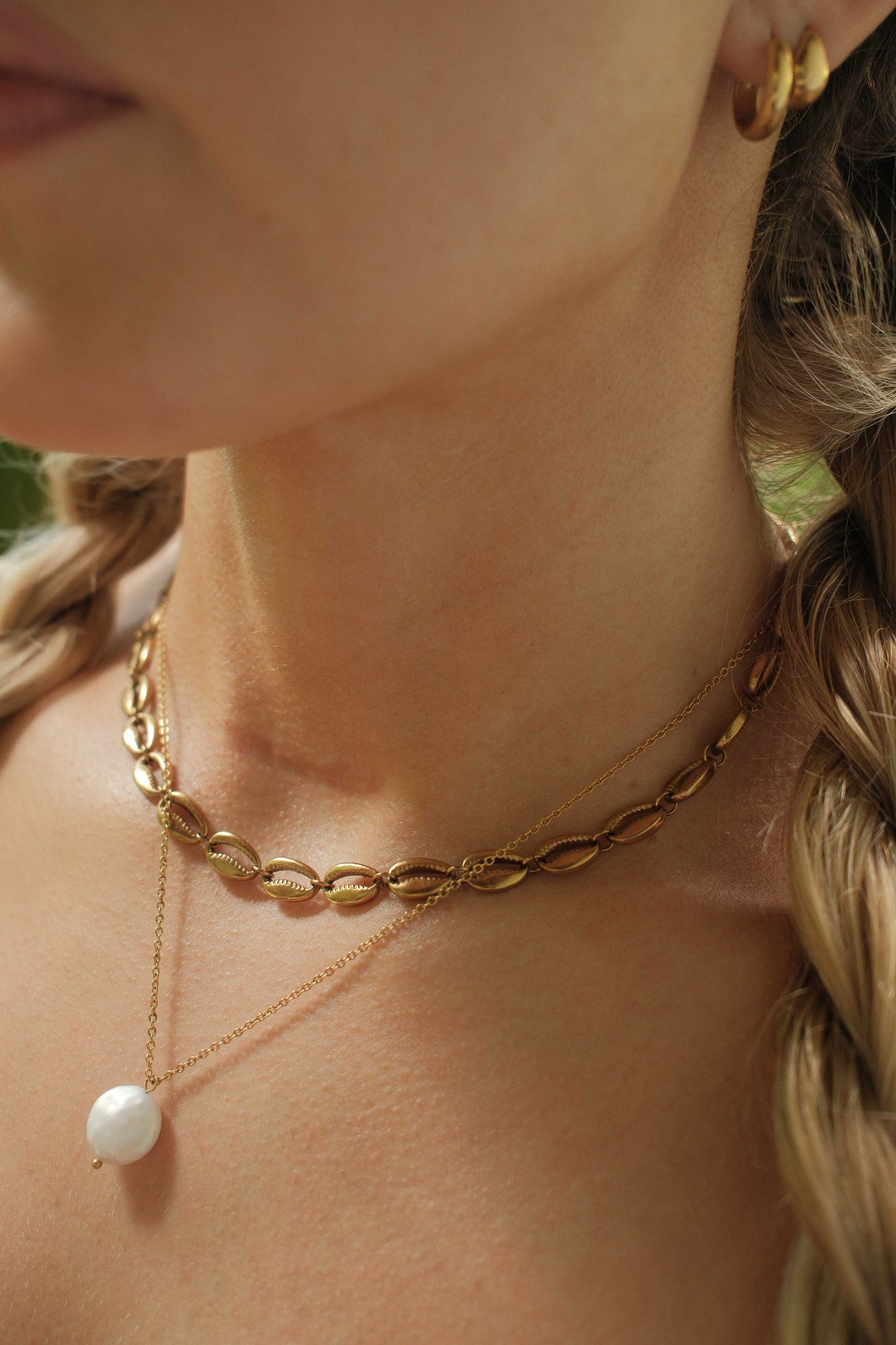 Close-up of a person wearing a gold chain necklace with a pearl pendant.