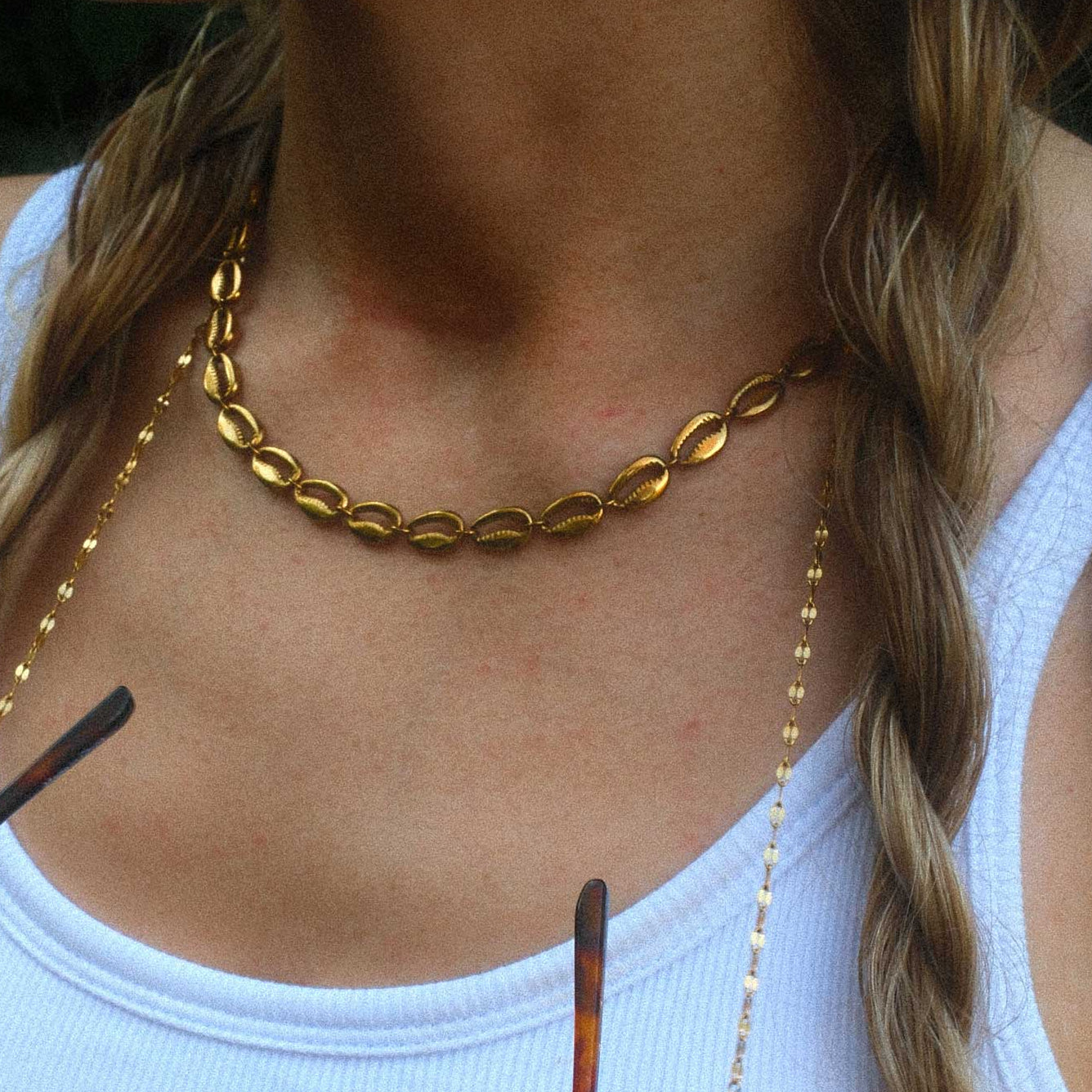 Woman wearing a gold choker necklace and holding sunglasses with a blurred background