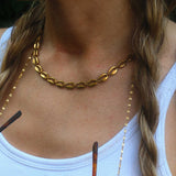 Woman wearing a gold choker necklace and holding sunglasses with a blurred background