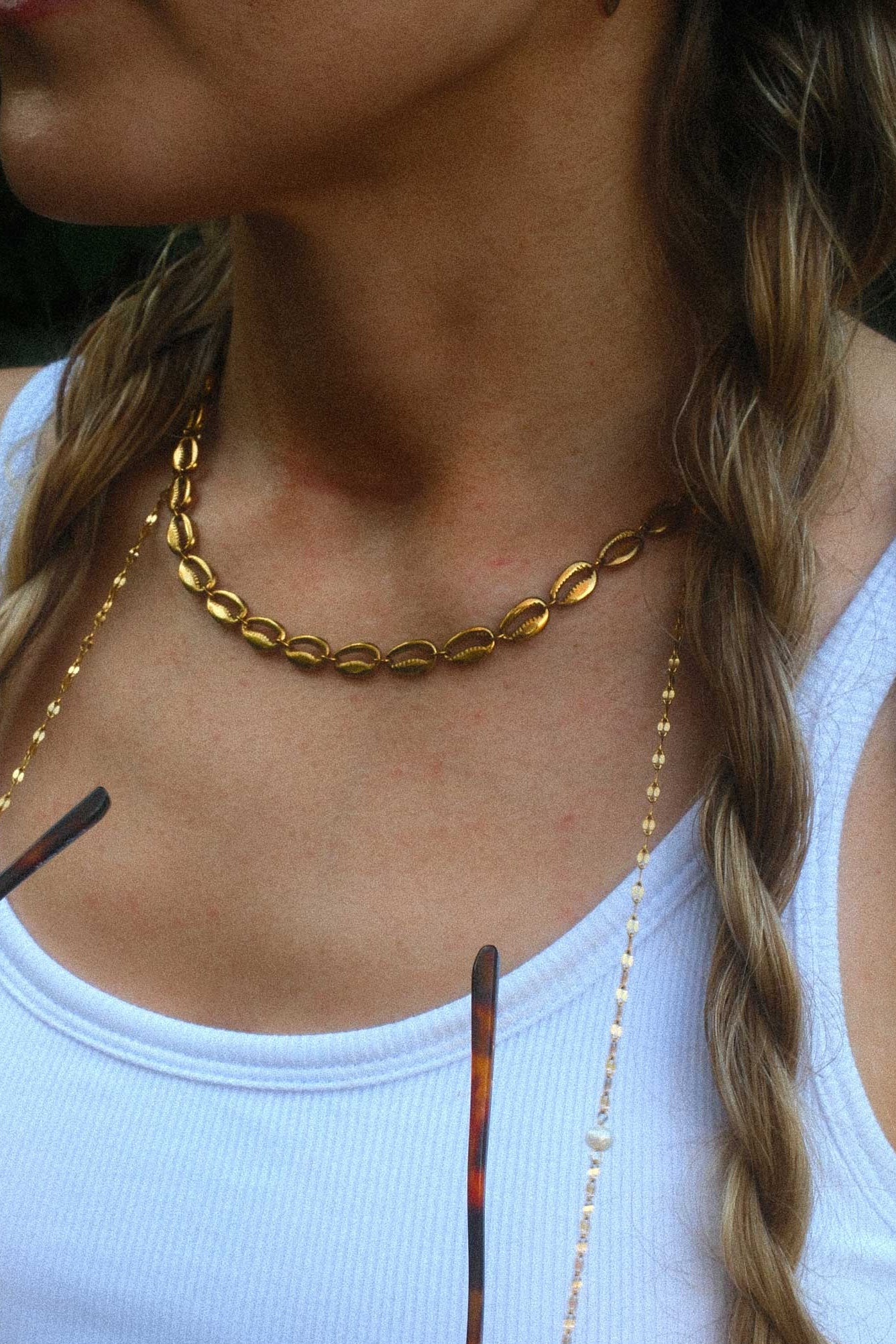 Woman wearing a gold choker necklace and holding sunglasses with a blurred background