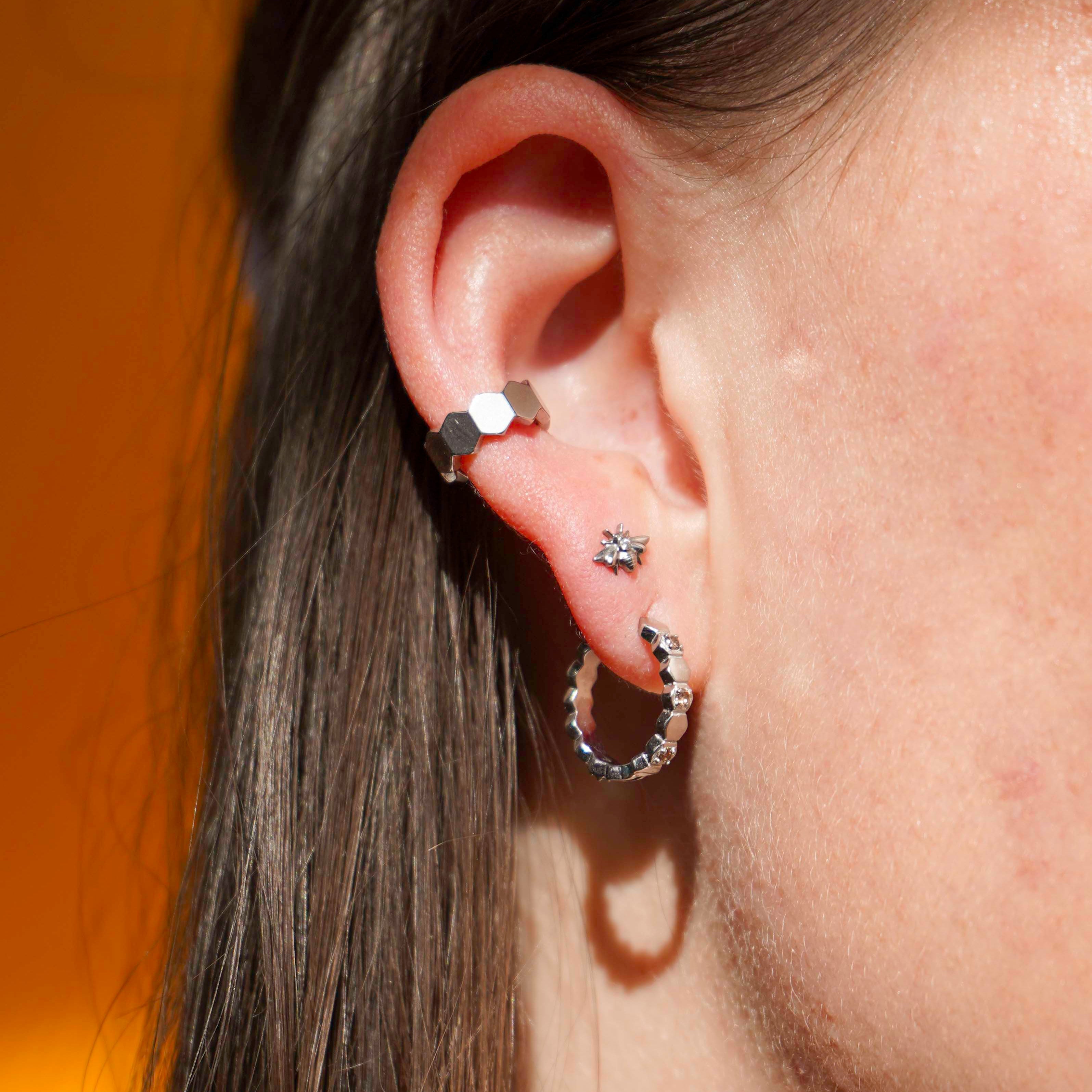 Close up of a model wearing a cuff earring made from stacked hexagon shapes. Hoop made from 18k gold-plated stainless steel.