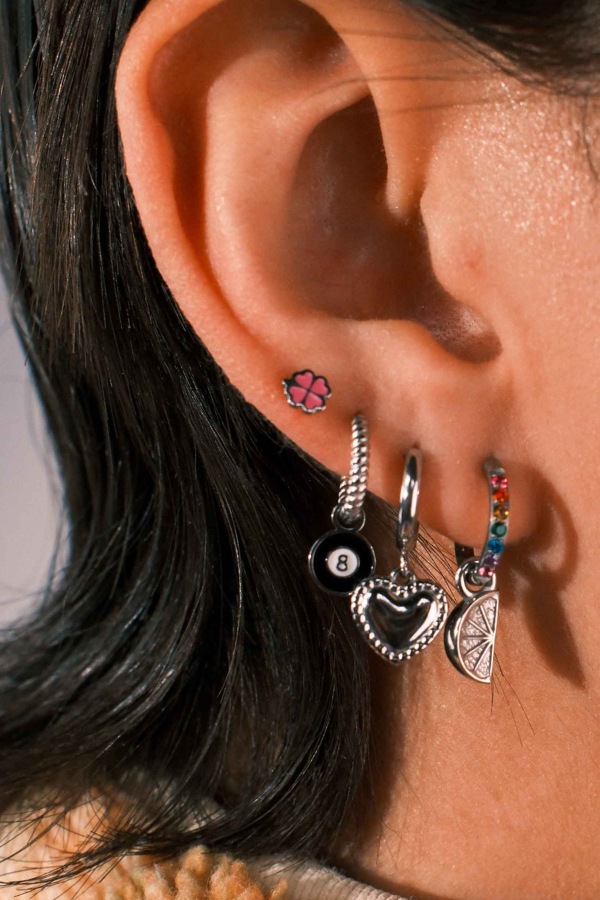 Close-up of an ear with multiple earrings including a black eight-ball charm and colorful hoop.