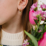 A close up of a bumblebee shaped hoop charm with yellow and black enamel and gold-plated titanium metal hanging from a hoop earring.