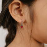 A close up of a ladybug shaped hoop charm with red and black enamel and  titanium metal hanging from a hoop earring.