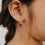 A close up of a ladybug shaped hoop charm with red and black enamel and  titanium metal hanging from a hoop earring.