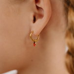 A close up of a ladybug shaped hoop charm with red and black enamel and gold-plated titanium metal hanging from a hoop earring.