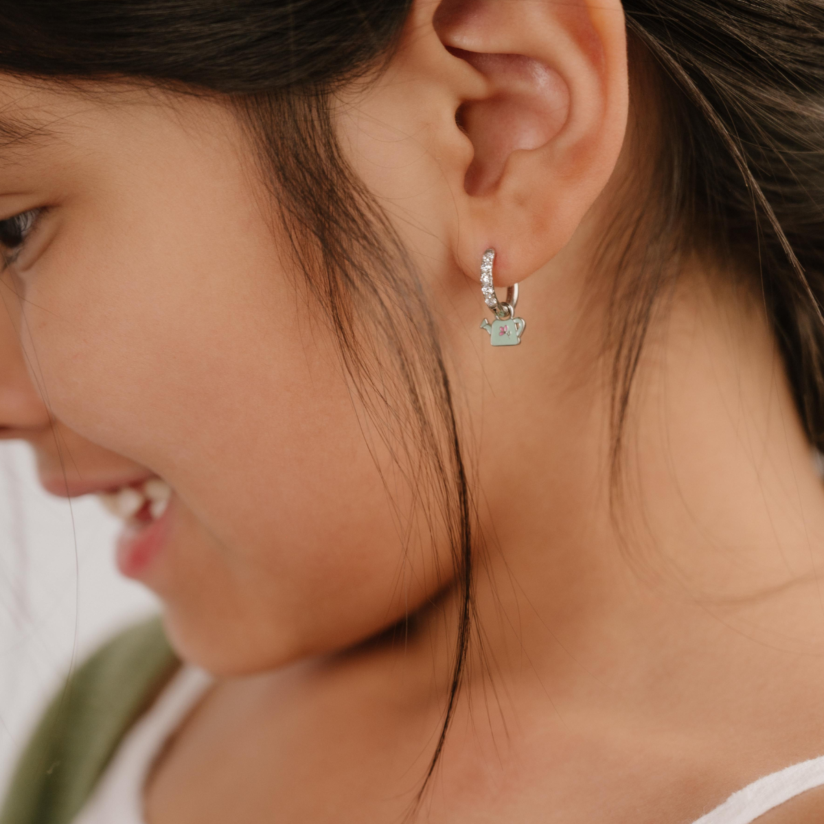 A close up of a right-facing watering can shaped charm with mint green enamel and titanium metal hanging from a hoop earring.