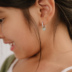 A close up of a right-facing watering can shaped charm with mint green enamel and titanium metal hanging from a hoop earring.