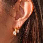 Close-up of an ear wearing gold and crystal earrings with a blurred background