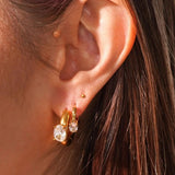 Close-up of an ear wearing gold and crystal earrings with a blurred background