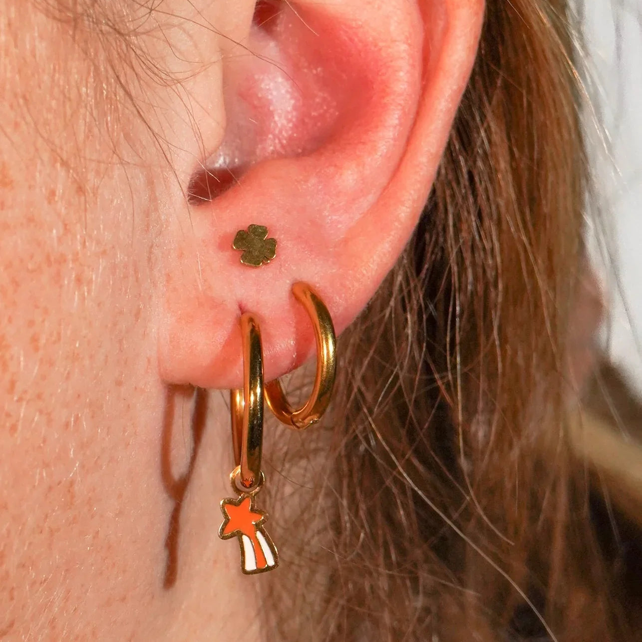Close-up of an ear wearing gold hoop earrings with star and clover charms.