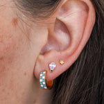 Close-up of an ear wearing colorful hoop earrings with a star and hot air balloon design.