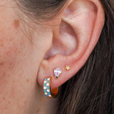 Close-up of an ear wearing colorful hoop earrings with a star and hot air balloon design.