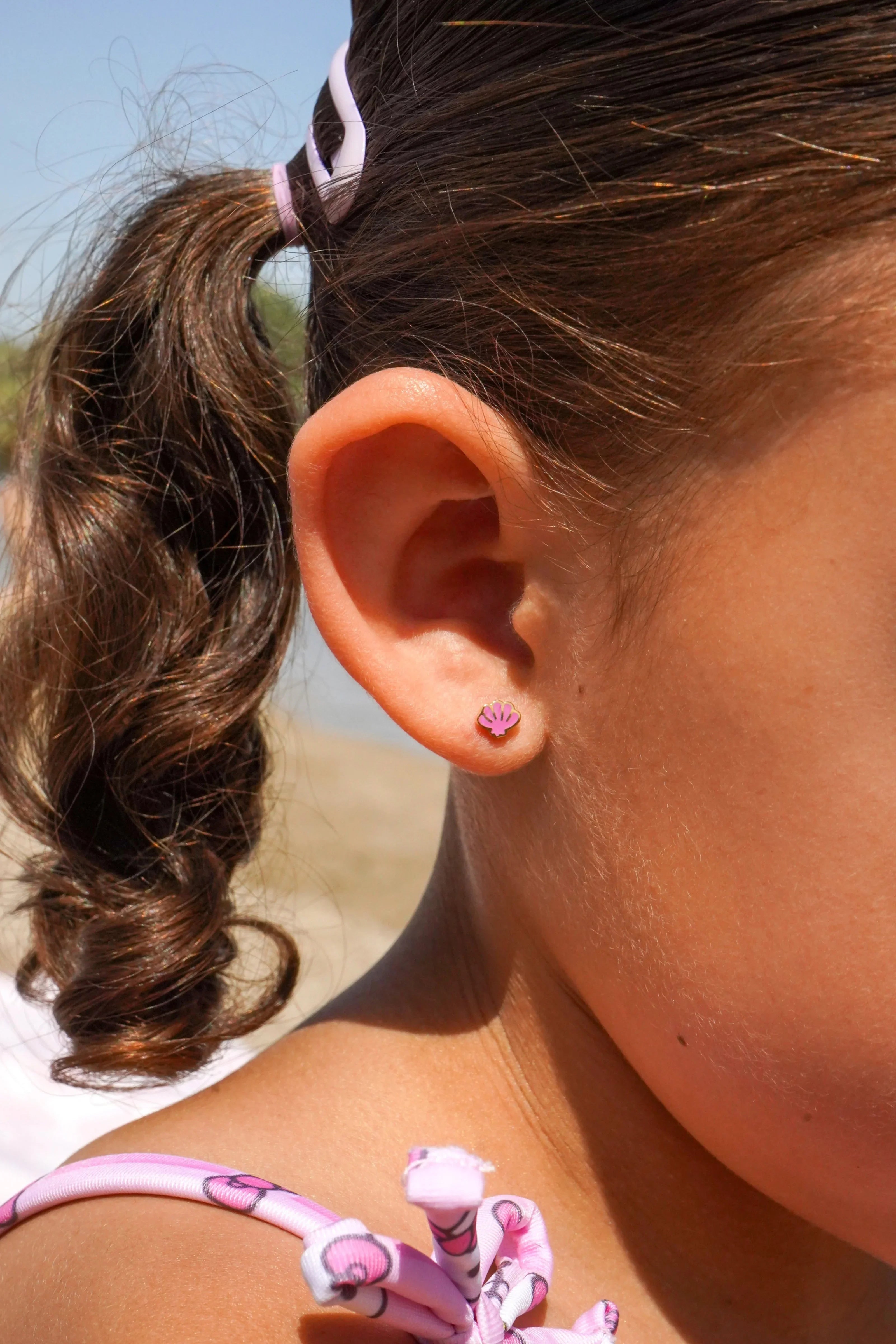 Close-up of a girl's ear with purple earring on a beach.