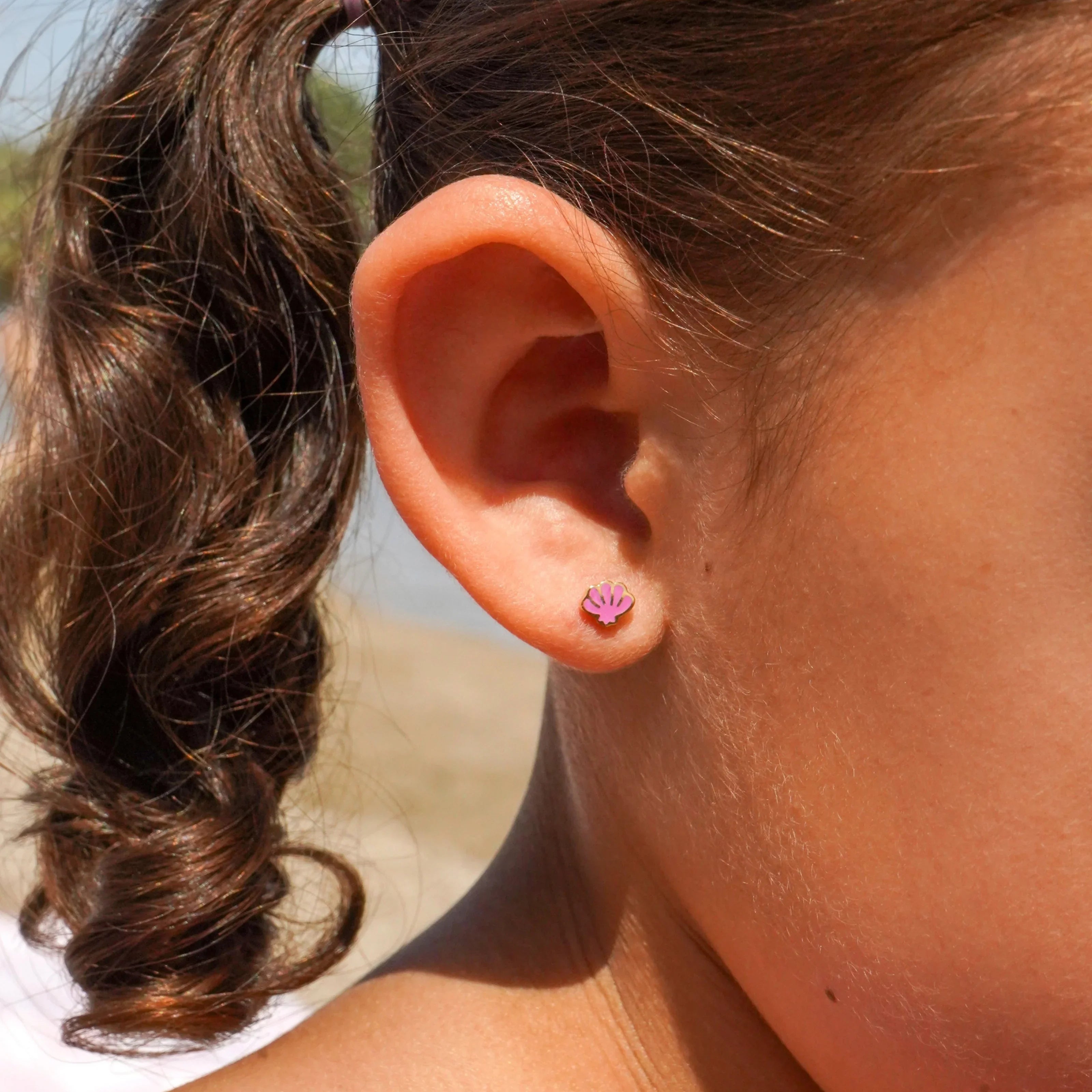 Close-up of a girl's ear with purple earring on a beach.