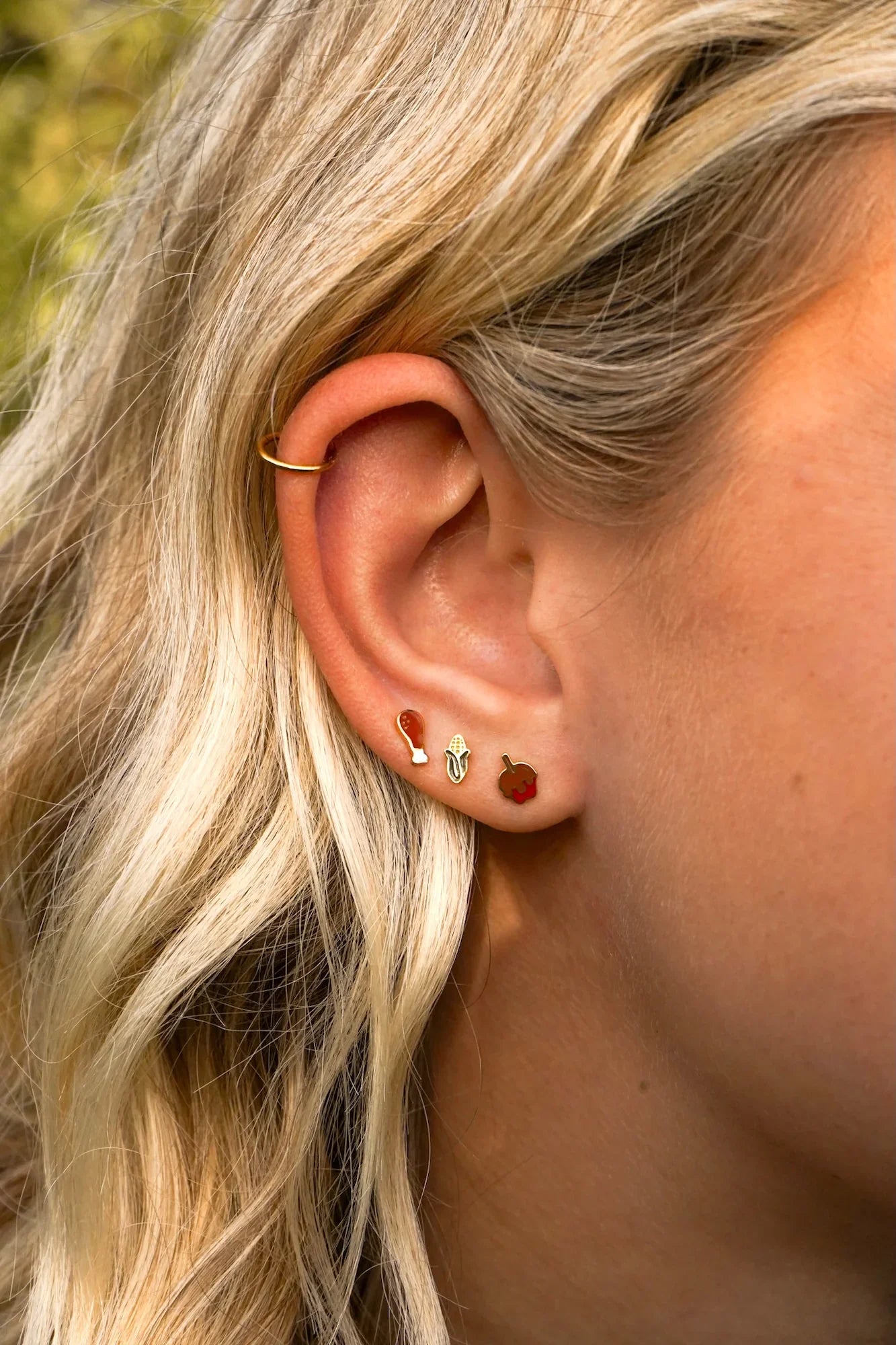 Close-up of a person's ear with multiple earrings against a blurred natural background